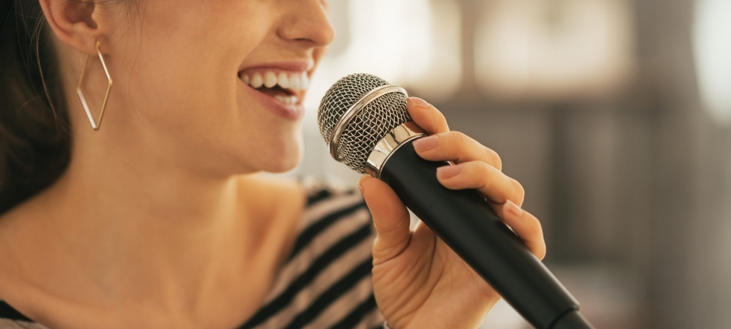 Closeup on happy young woman singing with microphone